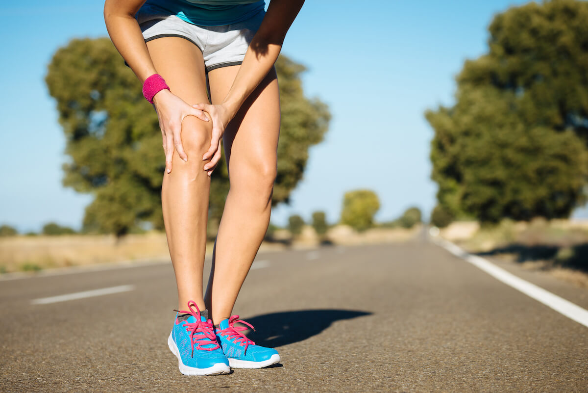 Woman running stops to hold her knee in pain